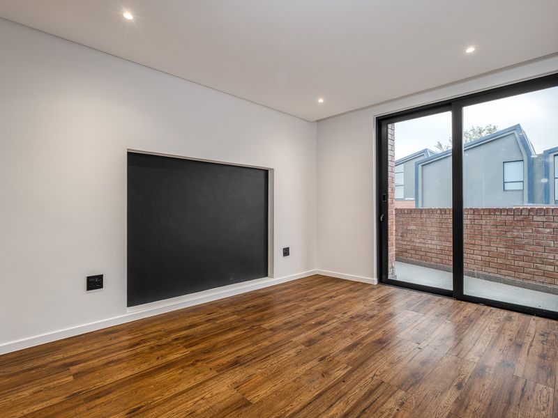A bright, modern living area featuring laminate wood flooring, recessed lighting, and a large sliding glass door leading to an outdoor space.