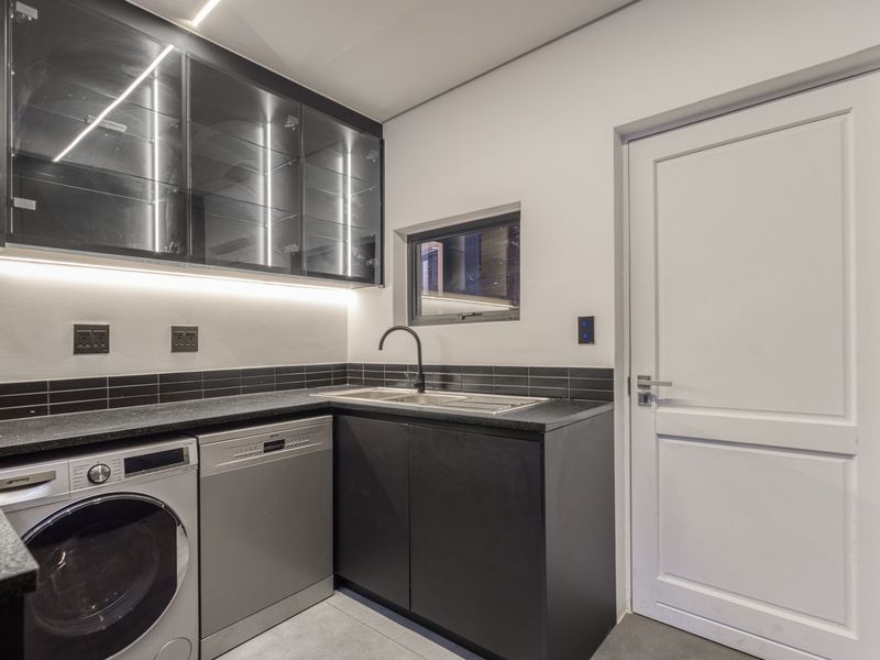 Modern scullery featuring sleek black cabinetry, stone countertops, integrated sink, and under-cabinet lighting, providing a functional and stylish utility space.