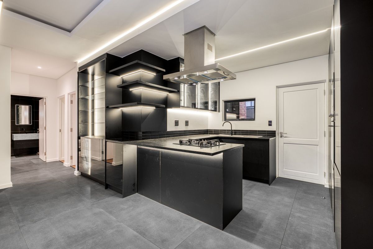 Modern, high-end kitchen featuring sleek black cabinetry, stone countertops, integrated gas hob, extractor fan, and contemporary recessed lighting throughout.
