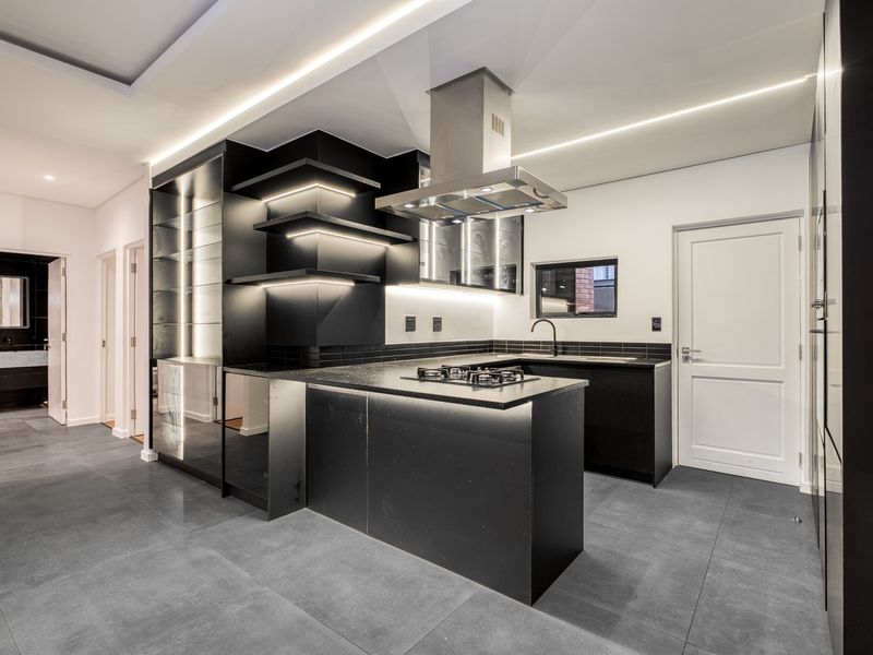Modern, high-end kitchen featuring sleek black cabinetry, stone countertops, integrated gas hob, extractor fan, and contemporary recessed lighting throughout.