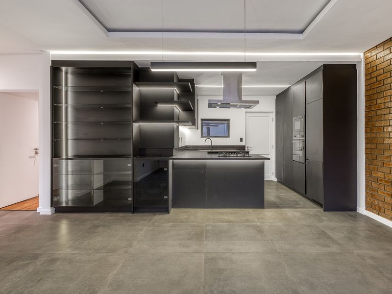 Modern, high-end kitchen featuring sleek dark cabinetry, a central island with integrated cooktop, built-in appliances, and a striking exposed brick feature wall.