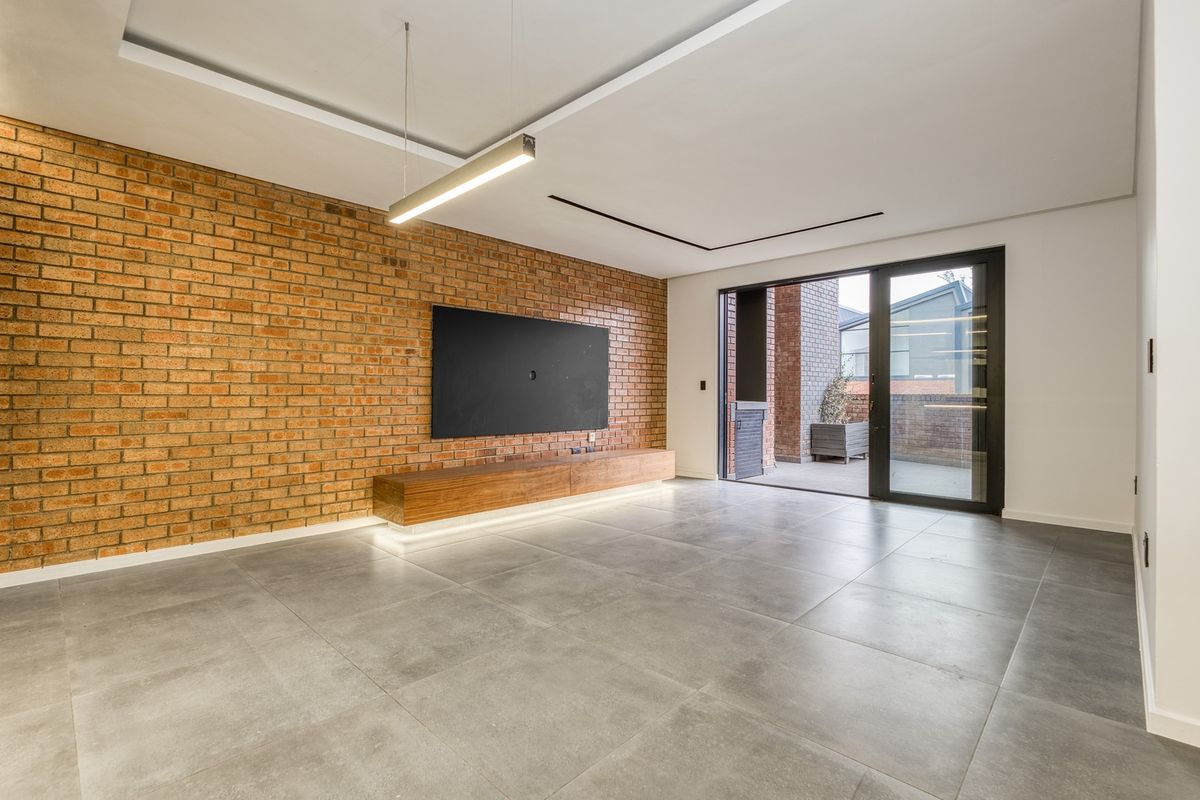 Modern living room featuring an exposed brick feature wall, floating timber media console, large format floor tiles, and direct access to a private patio.