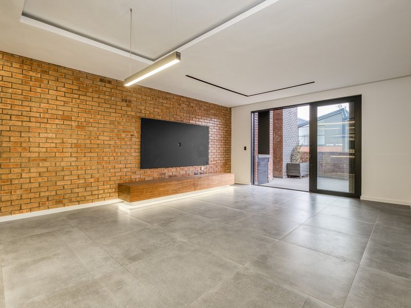 Modern living room featuring an exposed brick feature wall, floating timber media console, large format floor tiles, and direct access to a private patio.