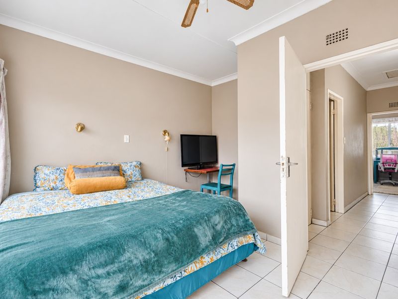 A bedroom featuring tiled flooring, a ceiling fan, and neutral wall tones, with an open doorway leading to a hallway.