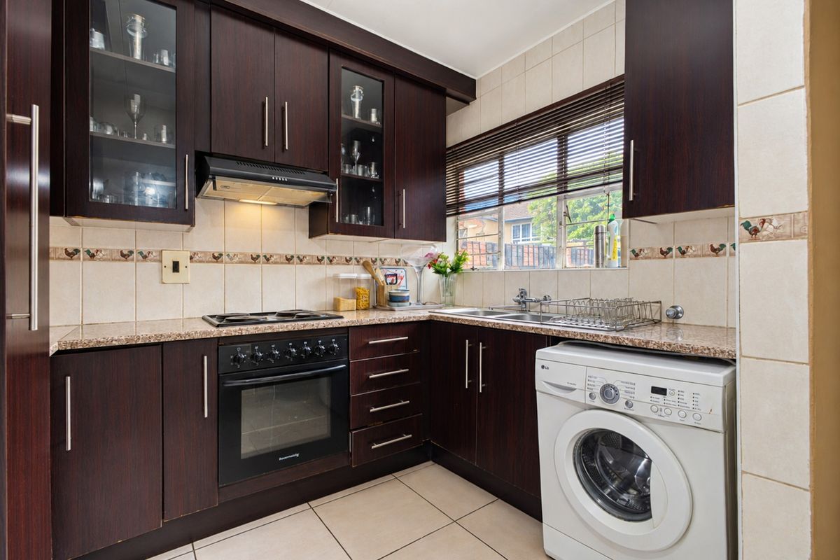 A functional kitchen featuring dark wood cabinetry, granite countertops, built-in oven, hob, extractor fan, and integrated laundry plumbing with tiled finishes.