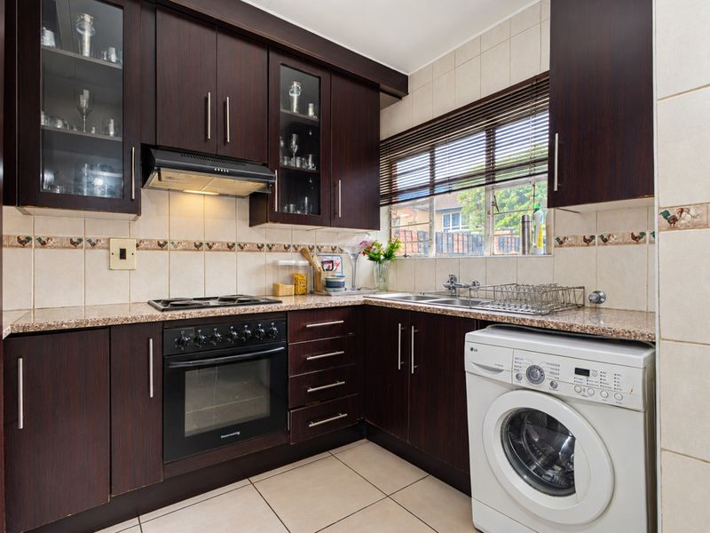 A functional kitchen featuring dark wood cabinetry, granite countertops, built-in oven, hob, extractor fan, and integrated laundry plumbing with tiled finishes.