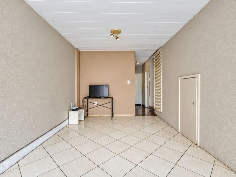 A spacious, neutral-toned living area featuring tiled flooring, a panelled ceiling, and a built-in storage cupboard, offering a blank canvas for interior design.