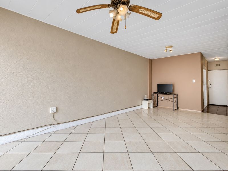 Spacious living area featuring neutral tiled flooring, a ceiling fan, and a simple layout, ready for personalization and minor cosmetic updates.