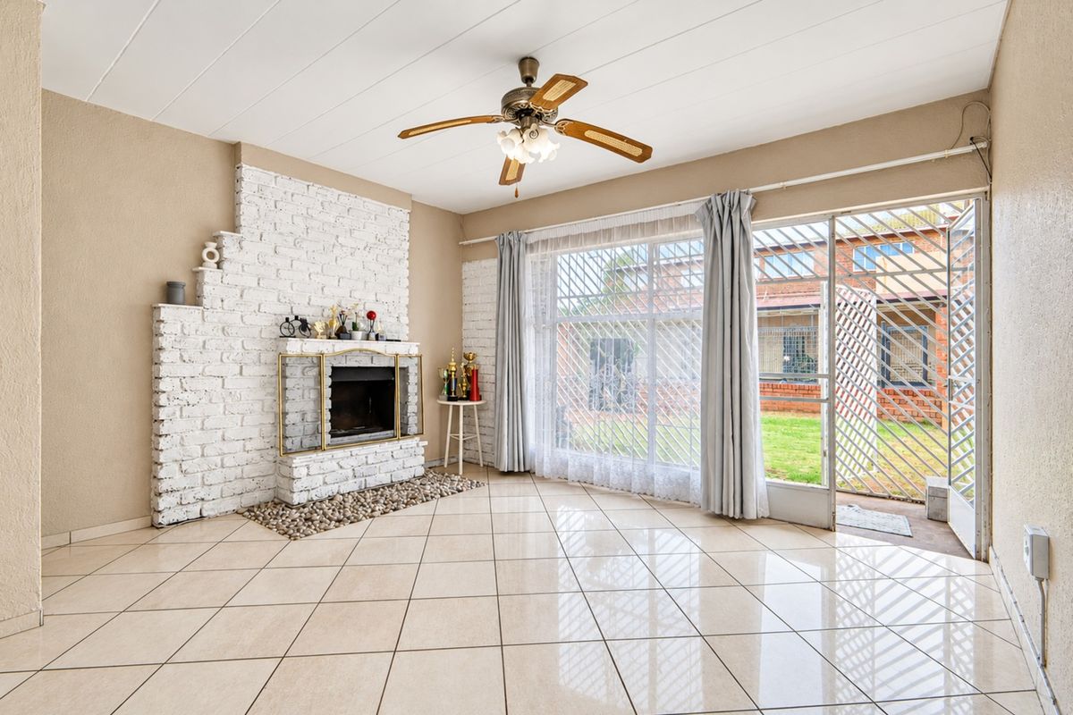 Spacious living room featuring a white brick fireplace, tiled flooring, and direct access to the outdoor area through a sliding glass door.
