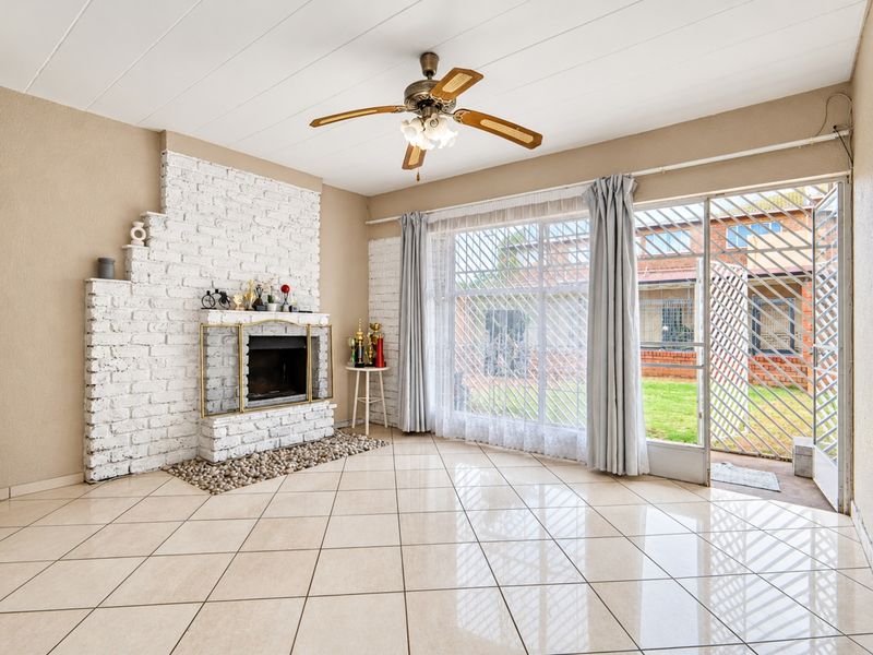 Spacious living room featuring a white brick fireplace, tiled flooring, and direct access to the outdoor area through a sliding glass door.