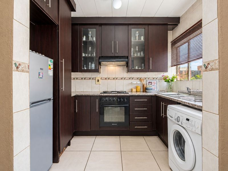 Compact kitchen featuring dark wood cabinetry, built-in oven with gas hob, extractor fan, tiled backsplash, and integrated space for laundry appliances.
