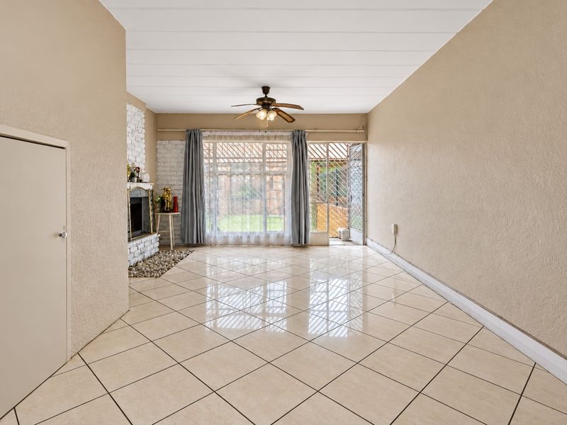 Spacious living room featuring tiled flooring, a brick fireplace, and a ceiling fan, with direct access to the outdoor area through a sliding glass door.