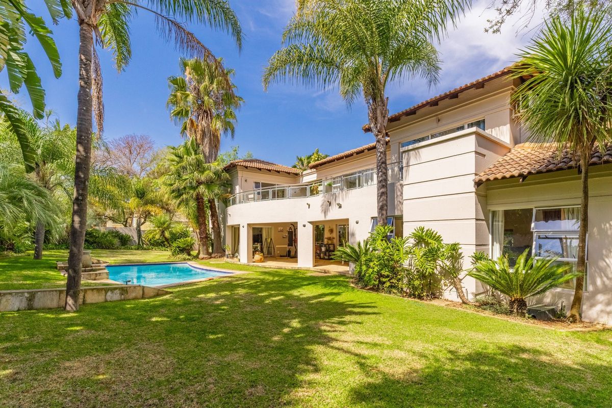 Rear view of the property featuring a well-maintained garden, swimming pool, and a spacious upper-level balcony with glass balustrades.