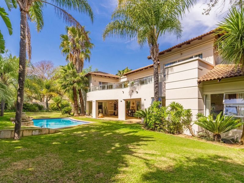Rear view of the property featuring a well-maintained garden, swimming pool, and a spacious upper-level balcony with glass balustrades.