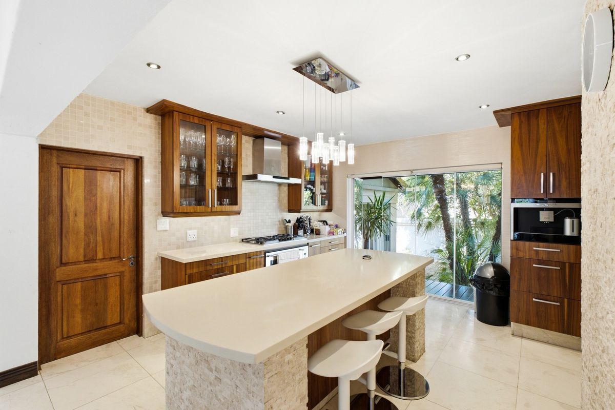 Modern kitchen featuring a central island with stone countertops, built-in appliances, mosaic tile backsplash, and direct access to an outdoor patio area.