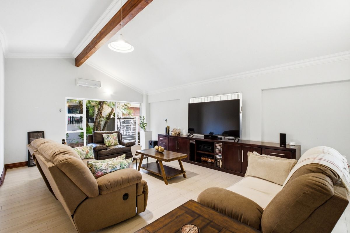 Spacious living room featuring a vaulted ceiling with an exposed timber beam, light-toned laminate flooring, and direct access to the outdoor area.
