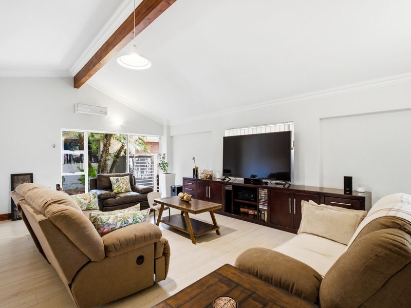 Spacious living room featuring a vaulted ceiling with an exposed timber beam, light-toned laminate flooring, and direct access to the outdoor area.