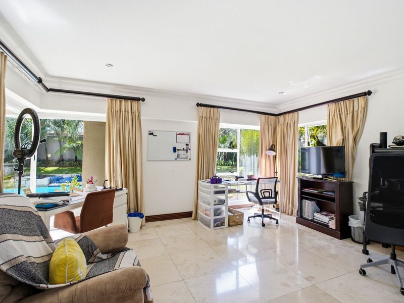 A bright home office featuring large windows, tiled flooring, and direct access to the outdoor pool area through sliding glass doors.