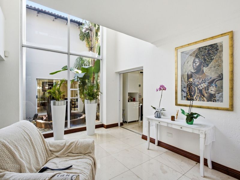 Bright living area featuring expansive floor-to-ceiling windows that provide a view into a private courtyard, complemented by neutral tiled flooring.