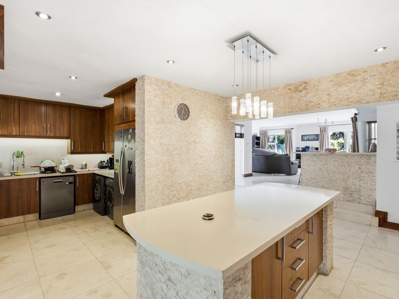 Spacious open-plan kitchen featuring a central island with stone countertop, modern cabinetry, and stone veneer accents, seamlessly flowing into the adjacent living area.