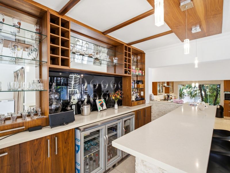 A sophisticated built-in home bar featuring custom wood cabinetry, stone countertops, integrated beverage coolers, and elegant coffered ceiling detailing.