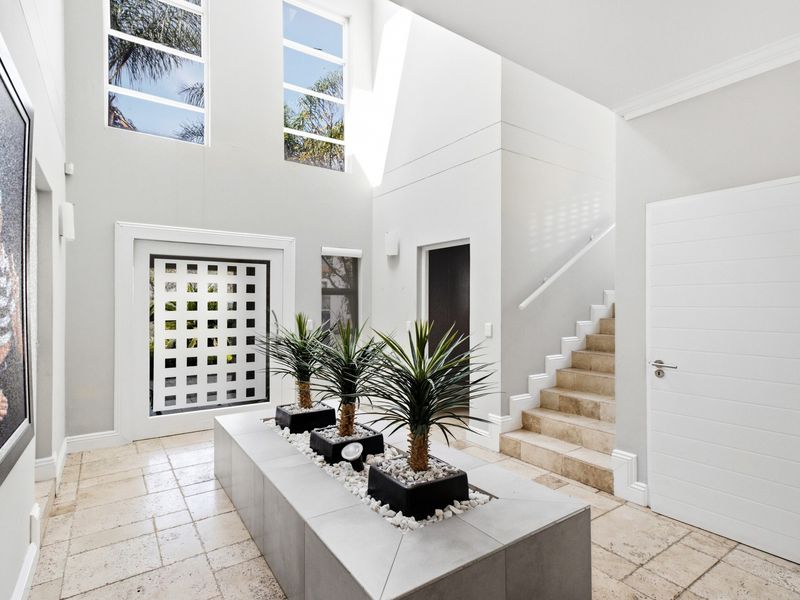 Spacious double-volume entrance hall featuring elegant travertine flooring, a central built-in planter feature, and a staircase leading to the upper level.
