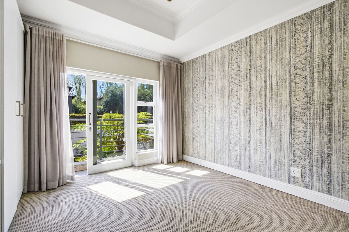 A bright, empty bedroom featuring a tray ceiling, textured feature wall, carpeted flooring, and a sliding glass door leading to an outdoor balcony.