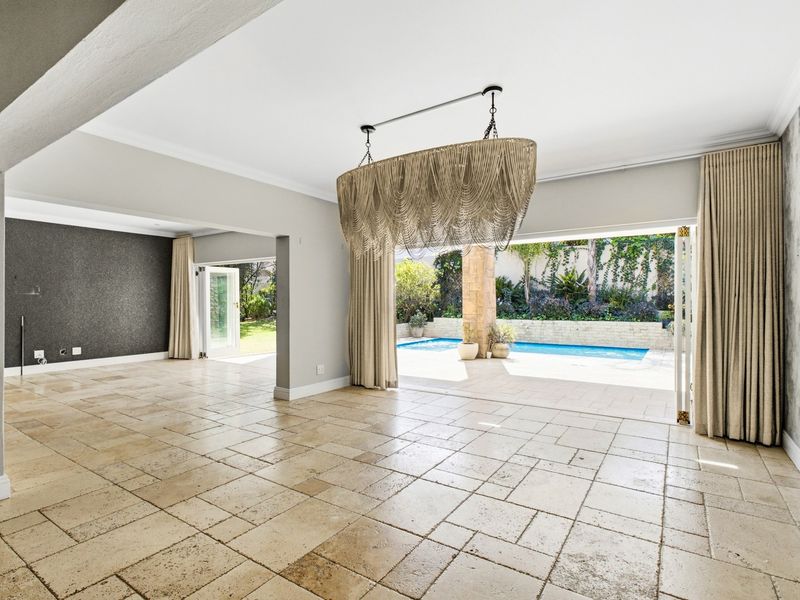 Spacious open-plan living area featuring travertine flooring and seamless indoor-outdoor flow through stacking doors to a private swimming pool and garden.