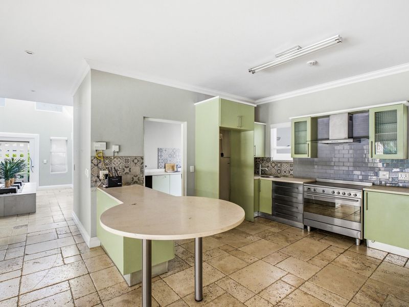 A functional kitchen featuring light green cabinetry, stainless steel appliances, a subway tile backsplash, and stone tile flooring with an integrated breakfast bar.