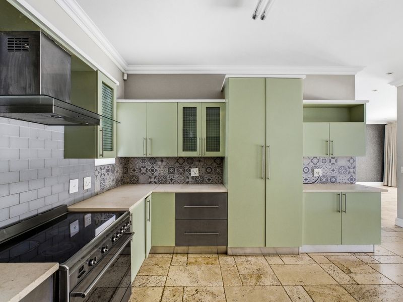 Modern kitchen featuring sage green cabinetry, stone countertops, tiled backsplash, and a professional-grade electric stove with an integrated extractor fan.