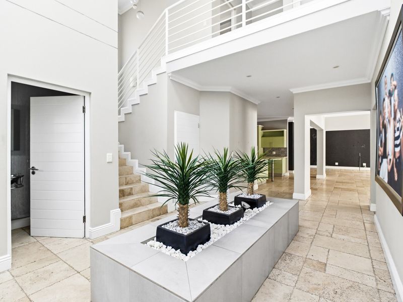 Spacious double-volume entrance hall featuring a central built-in planter, tiled flooring, and a staircase leading to an upper mezzanine level.
