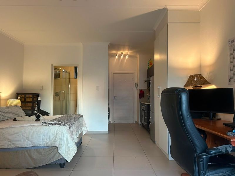 Open-plan studio apartment featuring tiled flooring, built-in storage, and an integrated bathroom with a shower enclosure.