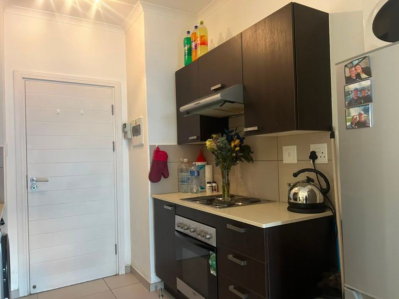 Compact kitchen featuring dark wood cabinetry, built-in oven, electric hob, extractor fan, and stone countertops with tiled splashback.