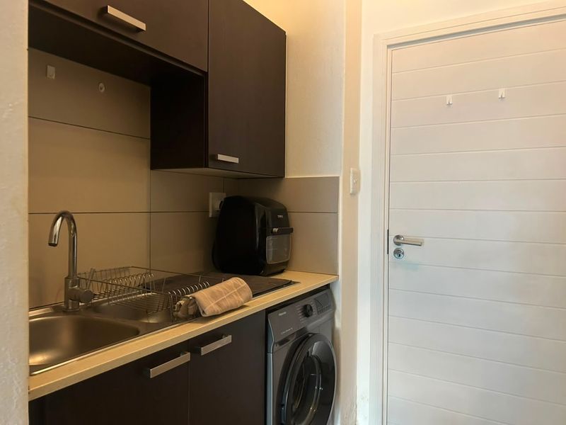 A compact laundry area featuring dark built-in cabinetry, a stainless steel sink with mixer tap, tiled splashback, and an integrated washing machine.