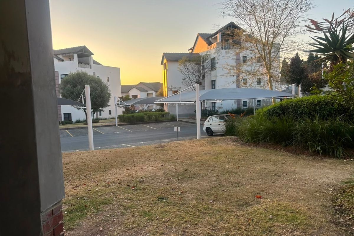 View of the apartment complex exterior featuring a paved parking area with shade-cloth carports and surrounding landscaped garden space.