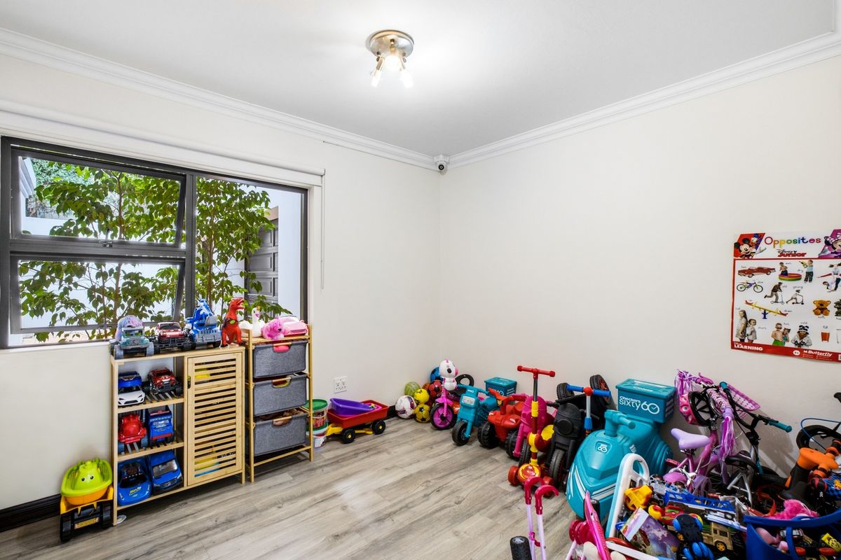 A bright bedroom featuring modern laminate flooring, decorative cornice, and an aluminium window frame, currently utilized as a play area.