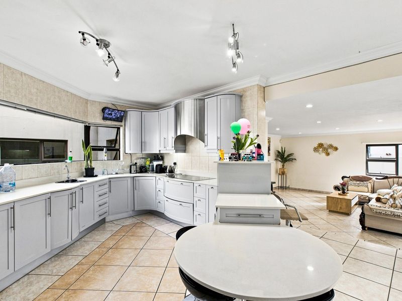 Spacious open-plan kitchen and living area featuring modern grey cabinetry, a central island, tiled flooring, and integrated kitchen appliances.