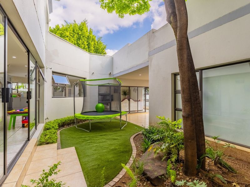 A private central courtyard featuring artificial turf, landscaped garden beds, and large sliding glass doors providing seamless indoor-outdoor flow.