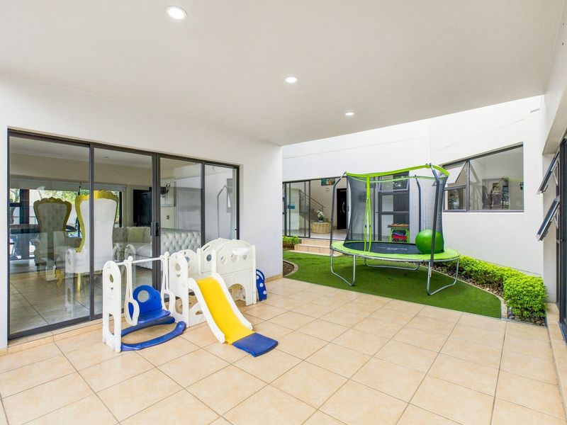 A spacious covered patio featuring tiled flooring, recessed lighting, and seamless access to the interior through large sliding glass doors.
