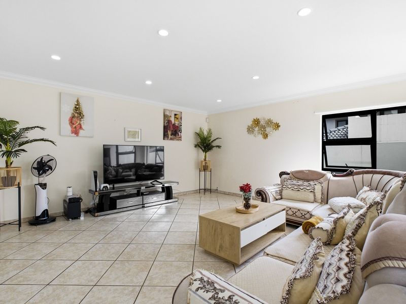 Spacious living room featuring neutral tiled flooring, recessed downlighting, and large aluminium-framed windows, providing a bright and comfortable area for relaxation.
