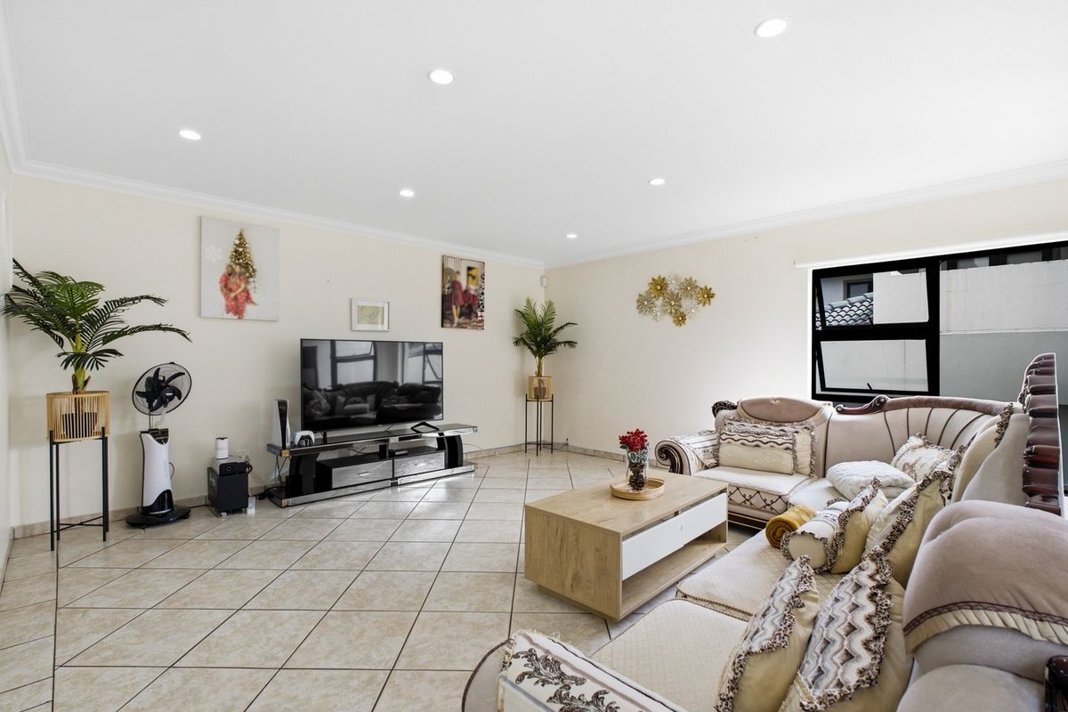 Spacious living room featuring neutral tiled flooring, recessed downlighting, and large aluminium-framed windows, providing a bright and comfortable area for relaxation.