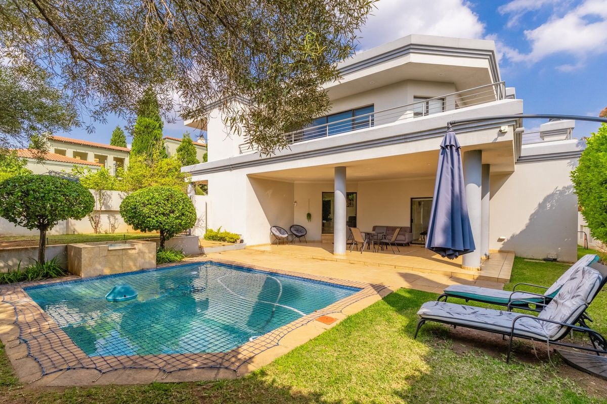 Rear view of a two-story house featuring a covered patio, swimming pool with safety net, and a well-maintained garden area.