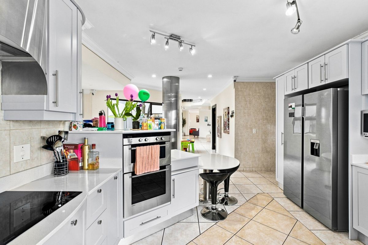 Modern kitchen featuring white cabinetry, quartz countertops, built-in oven, electric hob, and tiled flooring, seamlessly flowing into the adjacent living area.