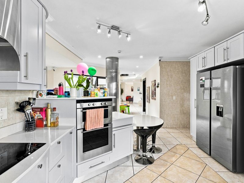 Modern kitchen featuring white cabinetry, quartz countertops, built-in oven, electric hob, and tiled flooring, seamlessly flowing into the adjacent living area.