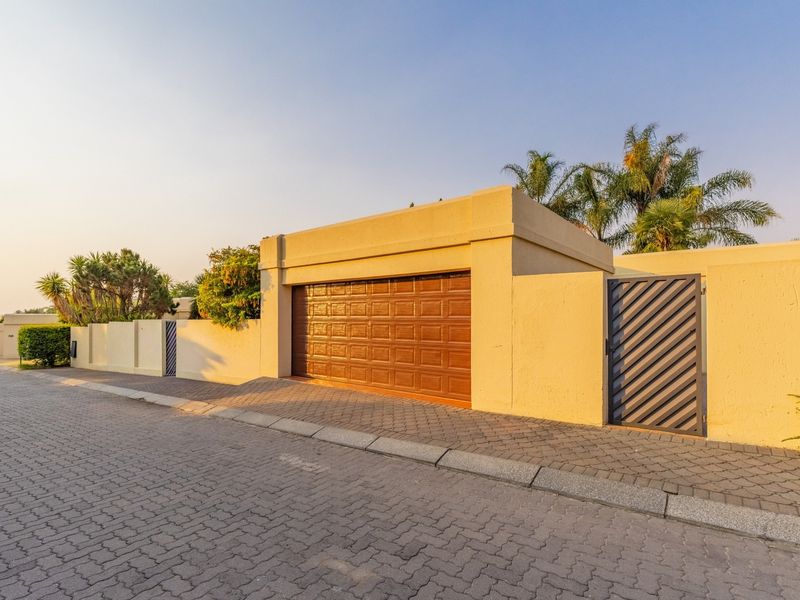 Street view of the property featuring a secure boundary wall, a brown sectional garage door, and a private pedestrian gate with paved driveway access.