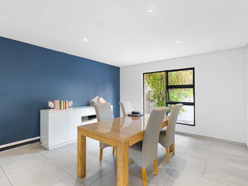 A bright dining room featuring large-format floor tiles, a striking blue accent wall, and a modern black-framed window overlooking the garden.