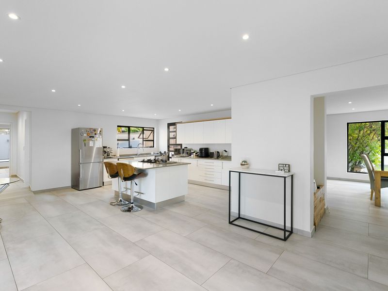 Modern open-plan kitchen featuring a central island, sleek white cabinetry, recessed lighting, and large format floor tiles, seamlessly connecting to the dining area.