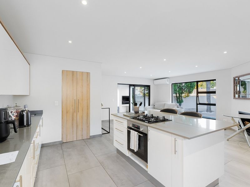 Modern open-plan kitchen and living area featuring a central island with gas cooktop, stone countertops, and seamless access to the outdoor patio.