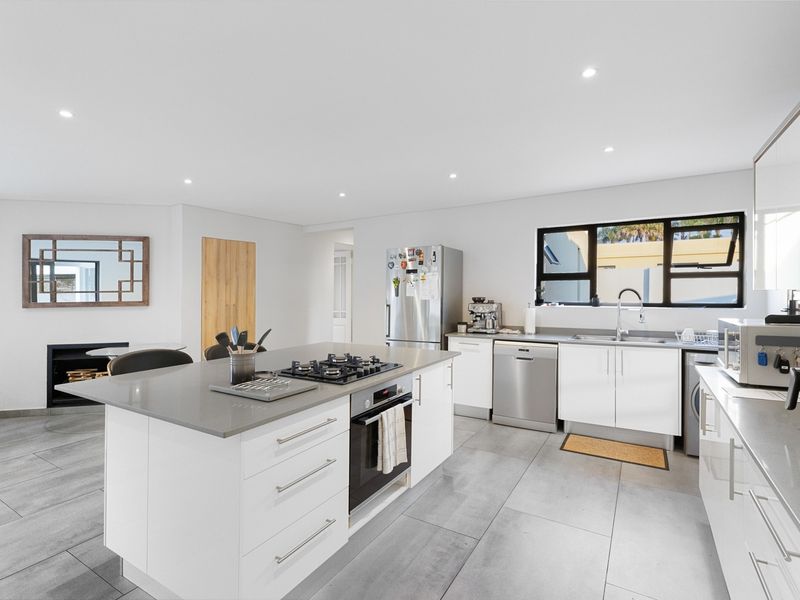 Modern open-plan kitchen featuring a central island with a gas hob, stone countertops, sleek white cabinetry, and large format floor tiles.
