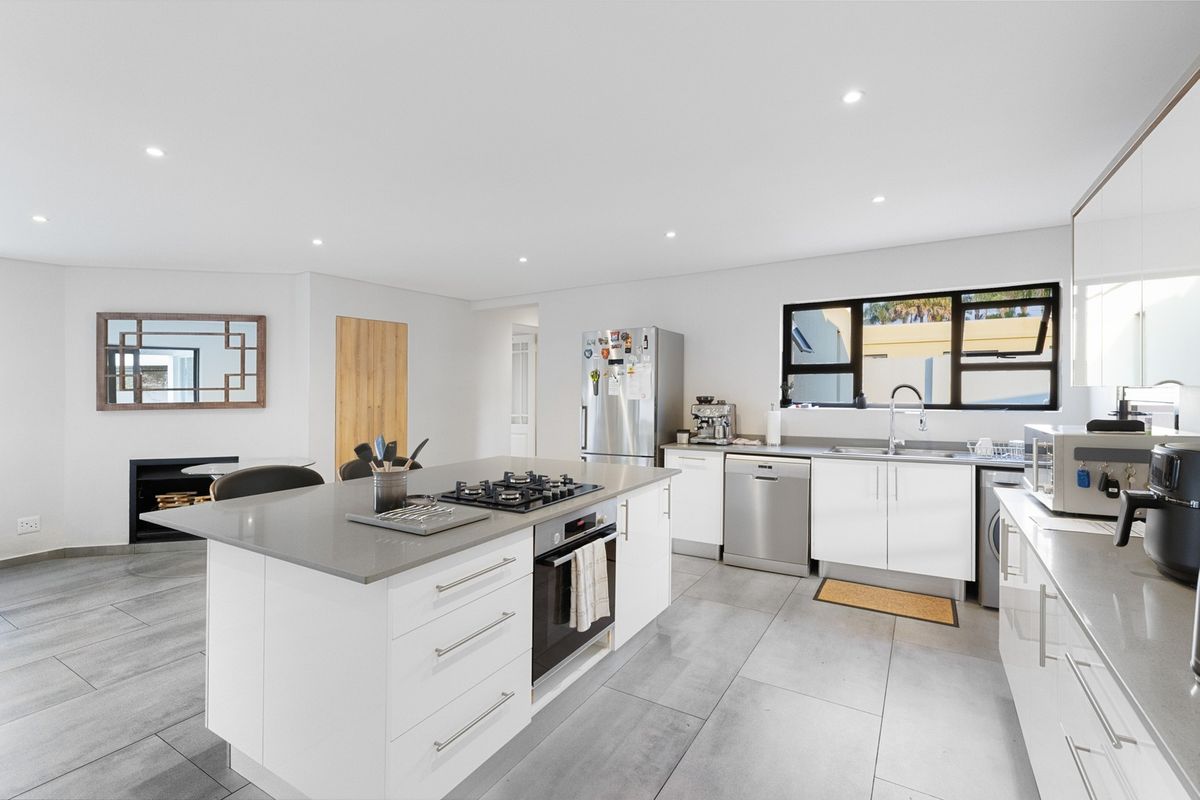 Modern open-plan kitchen featuring a central island with a gas hob, stone countertops, sleek white cabinetry, and large format floor tiles.